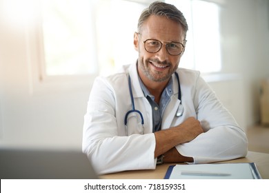 Portrait Of Mature, Doctor Sitting In Medical Office