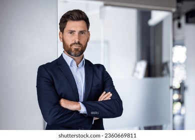 Portrait of mature experienced financier businessman, man thinking seriously looking at camera with crossed arms, confident investor banker inside office workplace in business suit.