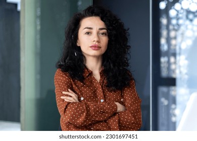 Portrait of mature female boss inside office building, successful hispanic woman looking serious at camera with crossed arms, businesswoman confident.