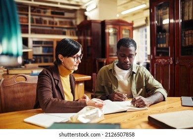 Portrait of mature female professor tutoring African-American student in classic library interior at college - Powered by Shutterstock