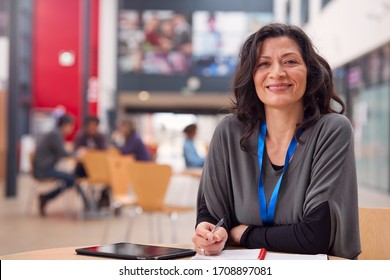 Портрет зрелой учительницы или студентки с цифровым планшетом, работающей за столом в зале колледжа