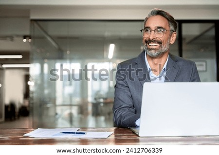 Portrait mature Indian, arabian business man ceo trader using laptop computer, working in modern office. Middle-age Hispanic smiling handsome businessman entrepreneur looking at copy space, dreaming