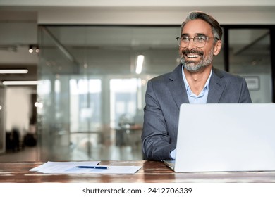 Portrait of mature Indian or Latin business man ceo trader using laptop computer, typing, working in modern office. Middle-age Hispanic smiling handsome businessman entrepreneur looking aside,dreaming - Powered by Shutterstock