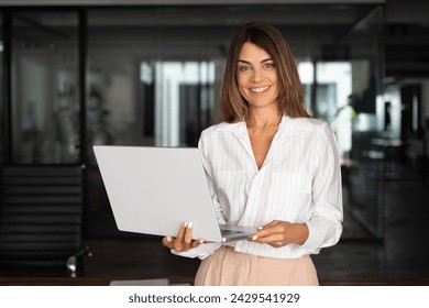 Portrait of mature Latin businesswoman ceo using computer, working in modern office. 40 years old woman doing online business data market analysis, planning tech strategy looking at camera, copy space - Powered by Shutterstock