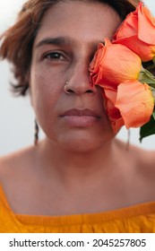 Portrait Of A Mature Latina Woman With An Orange Flower Looking At The Camera.