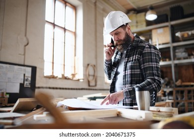 Portrait of mature male carpenter looking at blueprints plans and making a phone call in carpentery workshop. Small business concept. - Powered by Shutterstock