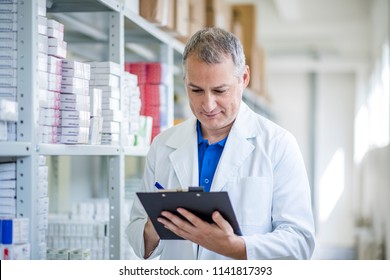 Portrait Of Mature Male Pharmacists Working In Modern Drugstore. Medical Factory Supplies Storage Indoor With Male Pharmacists. Pharmacist Man In The Warehouse Holding Boxes With Drugs In Hands