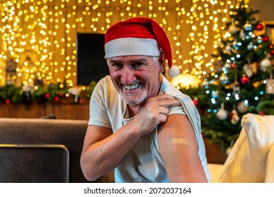 Portrait Of A Mature Male Smiling After Getting A Vaccine - Man Showing Her Arm With Bandaid During A Christmas Party Dressing Red Cap