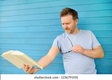 Portrait of mature man with big black eye glasses trying to read book but having difficulties seeing text because of vision problems. Hyperopia, presbyopia. - Powered by Shutterstock - Get 15% off with code: PIKWIZARD15