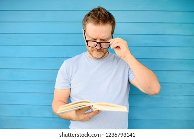 Portrait of mature man with big black eye glasses trying to read book but having difficulties seeing text because of vision problems. Problems disorder vision.
