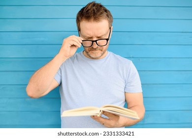 Portrait of mature man with big black eye glasses trying to read book but having difficulties seeing text because of vision problems. Problems disorder vision. - Powered by Shutterstock