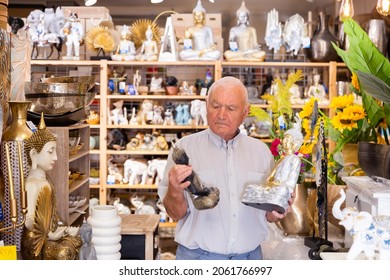 Portrait Of Mature Man Choosing Small Buddha Statue For Home Decor At Store Of Household Goods