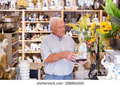 Portrait Of Mature Man Choosing Small Buddha Statue For Home Decor At Store Of Household Goods