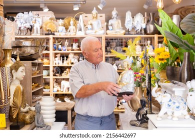 Portrait Of Mature Man Choosing Small Buddha Statue For Home Decor At Store Of Household Goods