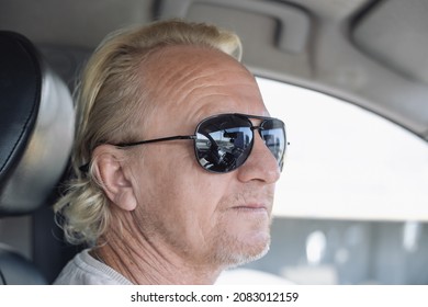 Portrait Of A Mature Man. A European, With Blond Hair Slicked Back, Wearing Sunglasses, Driving A Car.