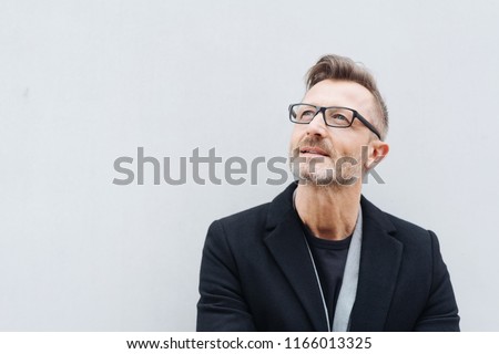Portrait of mature man with glasses wearing black coat looking up while standing against white background