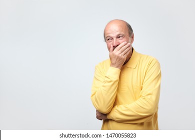 Portrait Of Mature Man Laughing And Covering His Mouth With Hand Over White Background. Trying To Hold A Laugh Not To Offend Some Person. He Just Heard A Funny Joke