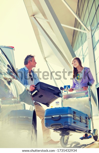 Portrait of mature man putting luggage on car trunk\
with lens flare