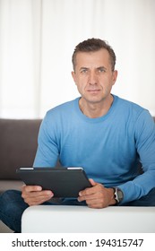 Portrait of mature man relaxing at home in sofa with tablet