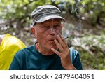 portrait of mature man smoking a cigarette in mountain woods dressed in hat and sports clothes and backpack