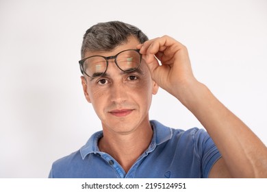 Portrait Of Mature Man Taking Off Eyeglasses Looking At Camera. Caucasian Man Wearing Blue T-shirt Standing Over White Background. Vision Correction Concept