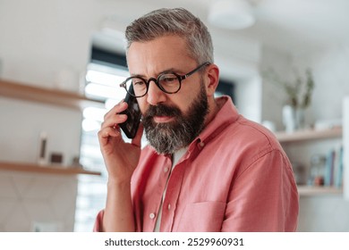 Portrait of mature man working from home phone calling, standing by kitchen island. Concept of remote work from home. Hygge at work. - Powered by Shutterstock