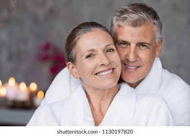 Portrait of mature married couple embracing with bathrobe and looking at camera. Happy senior man and beautiful woman in robes smiling at wellness center. Man and wife relaxing together at day spa.
