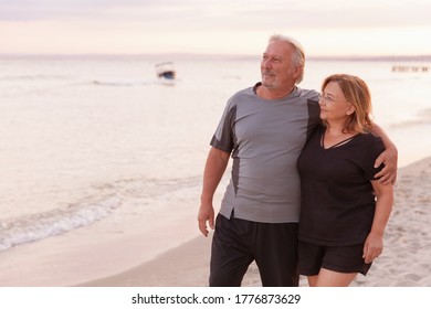 Portrait of mature married man and woman hugging each other while laughing. Senior couple enjoying beach holiday. 