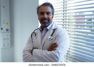 Portrait Of Mature Mixed Race Male Doctor Standing With Arm Crossed And Looking At Camera In Clinic At Hospital