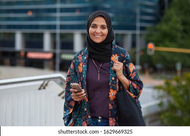 Portrait mature muslim woman smiling confident holding smartphone in city wearing traditional hijab headscarf