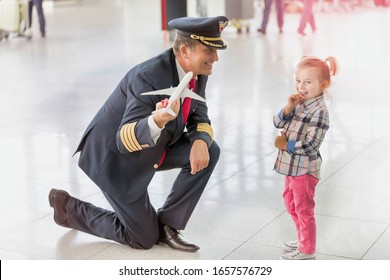 Portrait Of Mature Pilot Holding Airplane Toy While Playing With Cute Little Girl In Airport