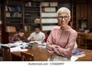 Portrait of mature professor standing in university library and looking at camera with copy space. Happy senior woman at the library working as a librarian. Satisfied college teacher smiling. - Powered by Shutterstock