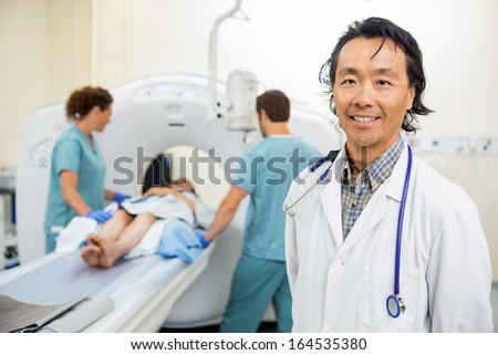 Portrait of mature radiologist with nurses preparing patient for CT scan in hospital