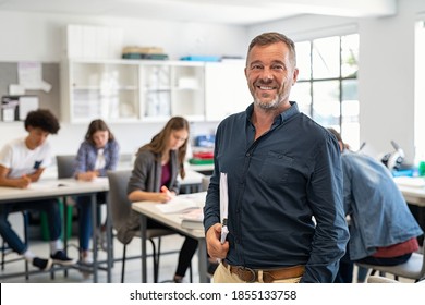 Portrait of mature teacher looking at camera with copy space. Happy mid adult lecturer at classroom standing after giving lecture. Satisfied high school teacher smiling while his students studying.