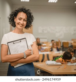 Portrait of mature teacher stand and hold clipboard with students in the background - Powered by Shutterstock