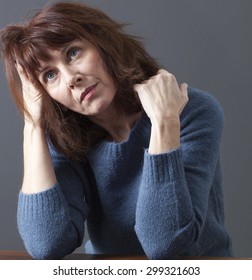 portrait of mature uncombed woman with brown hair and blue winter sweater thinking,head leaning on hand,looking imaginative