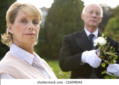 Portrait Of Mature Woman, Butler Pruning Bush In Background