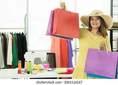 Portrait Mature Woman Costume Designer Smiling Confident Positive Holding Paper Bags Shopping. Asian Senior Woman Seamstress Owner Small Business Working At Workplace In Fashion Workshop. 