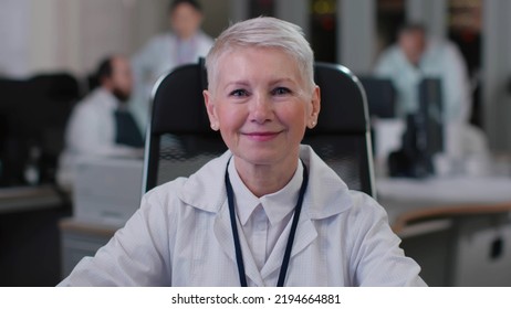 Portrait Of Mature Woman Doctor Smiling At Camera Sitting In Clinic Office. Female Scientist Posing At Camera Working In Modern Laboratory