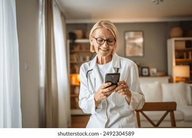 Portrait of mature woman doctor stand and use mobile phone at home - Powered by Shutterstock