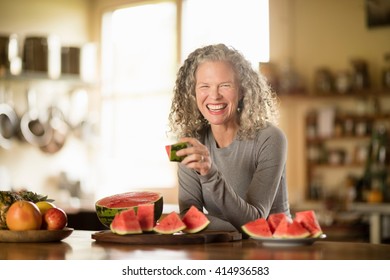 Portrait Of Mature Woman Eating Watermelon In Kitchen