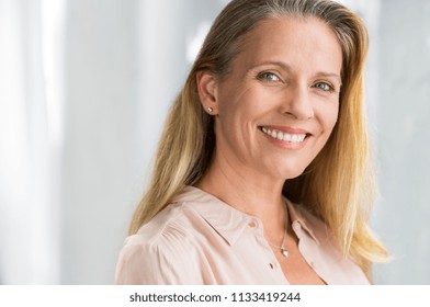 Portrait of mature woman enjoying life after retirement and looking at camera. Closeup face of happy senior woman with blond hair smiling. Beautiful smiling lady indoor.