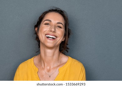 Portrait of mature woman laughing against grey background. Successful middle aged woman in casual with toothy smile looking at camera. Cheerful happy beautiful latin lady smiling with copy space.