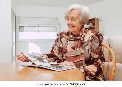 Portrait Of Mature Woman Looking At Pictures In The Album Made Many Years Ago. Grandmother Remembering Memories Of Family Members With Nostalgia And Melancholy.