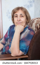Portrait of mature woman sitting in armchair with her head propped on hand and looking at camera, indoor