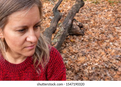 Portrait Of Mature Woman Sitting On Tree Trunk. Thought, Meditation Or Doubt Expression. Girl Does Not Look At Camera On Blurred Background With Copy Space. Relax Or Other Mental Psychology Concept