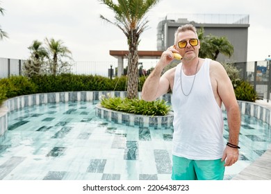 Portrait Of Mature Woman Standing At Swimming Pool And Talking On Banana