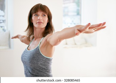 Portrait Of Mature Woman Stretching Her Arms And Looking Away At Gym. Beautiful Woman Performing Yoga In Warrior Pose, Virabhadrasana.