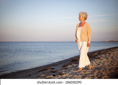 Portrait Of A Mature Woman Walking On The Beach Looking At The Sea. Relaxed Old Lady Strolling On The Beach With Lots Of Copyspace.