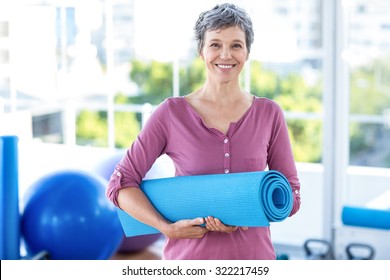 Portrait Of Mature Woman With Yoga Mat While Standing In Fitness Studio